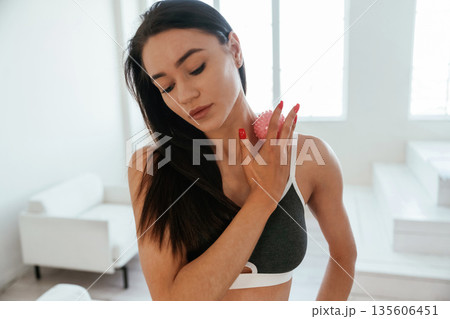 Doing massage by pink roller. Young woman with slim body type is indoors Doing massage by pink roller. Young woman with slim body type is indoors 135606451