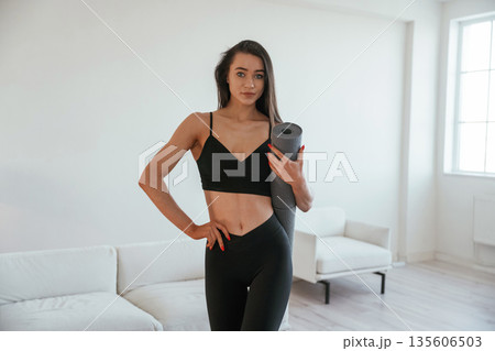 Ready for the yoga, holding mat. Young woman with slim body type is indoors Ready for the yoga, holding mat. Young woman with slim body type is indoors 135606503