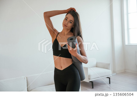 Ready for the yoga, holding mat. Young woman with slim body type is indoors Ready for the yoga, holding mat. Young woman with slim body type is indoors 135606504