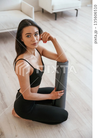 Taking a break, sitting with yoga mat. Young woman with slim body type is indoors Taking a break, sitting with yoga mat. Young woman with slim body type is indoors 135606510