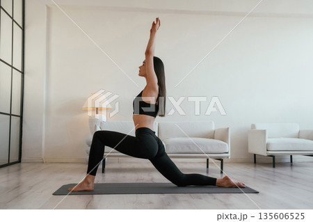 Asana on the yoga mat, with hands up. Young woman with slim body type is indoors Asana on the yoga mat, with hands up. Young woman with slim body type is indoors 135606525