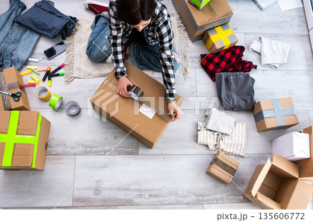 Girl Packs Cardboard Boxes And Takes Photos, Preparing Packages For Shipping Girl Packs Cardboard Boxes And Takes Photos, Preparing Packages For Shipping 135606772