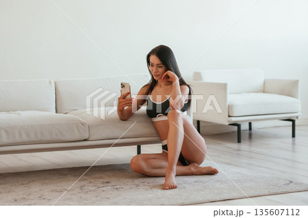 Social media, using smartphone, sitting on the floor. Young woman with slim body type is indoors Social media, using smartphone, sitting on the floor. Young woman with slim body type is indoors 135607112