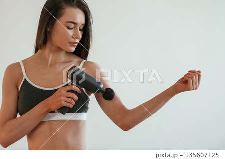 Process of doing self massage using massager. Young woman with slim body type is indoors 135607125