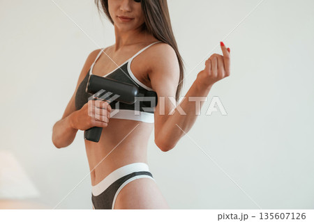 Process of doing self massage using massager. Young woman with slim body type is indoors Process of doing self massage using massager. Young woman with slim body type is indoors 135607126