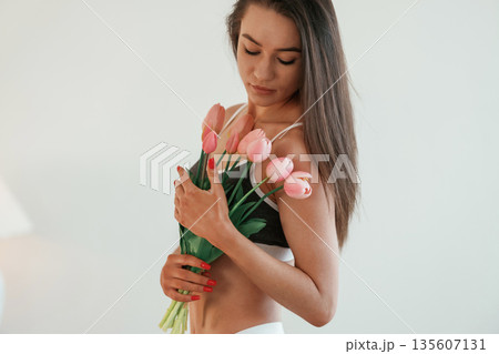 Gift of flowers in hands. Young woman with slim body type is indoors Gift of flowers in hands. Young woman with slim body type is indoors 135607131