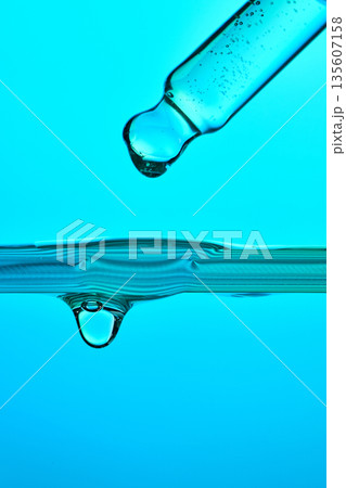 Pipette dropping blue liquid into water surface Pipette dropping blue liquid into water surface 135607158