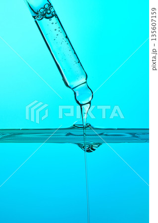 Dropper dispensing liquid into blue water surface 135607159