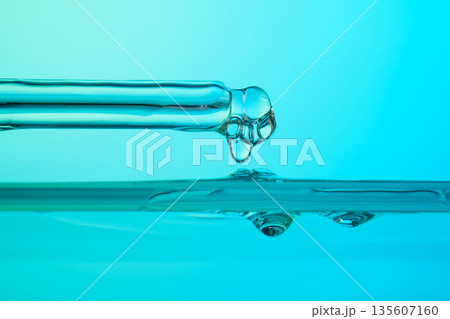 Pipette dripping blue liquid into water surface 135607160