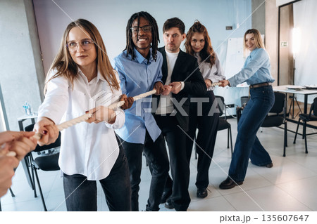 Tug of war game. Group of young business people are in conference room 135607647