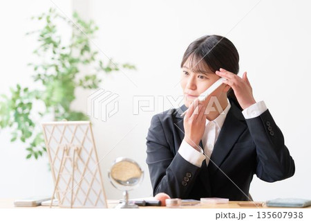 鏡を見ながらコームで前髪を整えて身だしなみチェックをするリクルートスーツ姿の女性 135607938