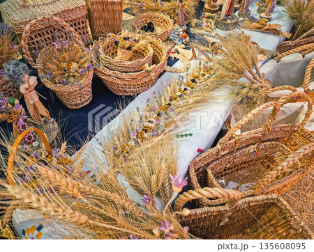 Causeni, Moldova - July 27, 2025: Traditional rustic crafts at an outdoor market. Various woven wicker baskets, intricate wheat sheaf arrangements and handmade folk dolls dressed in national costumes Causeni, Moldova - July 27, 2025: Traditional rustic crafts at an outdoor market. Various woven wicker baskets, intricate wheat sheaf arrangements and handmade folk dolls dressed in national costumes 135608095