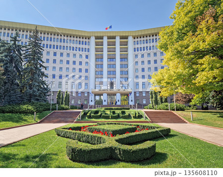 Chisinau, Moldova - September 24, 2025 Republic of Moldova parliament building with the Moldovan flag waving on the roof, and a large topiary garden with flowers in front Chisinau, Moldova - September 24, 2025 Republic of Moldova parliament building with the Moldovan flag waving on the roof, and a large topiary garden with flowers in front 135608110