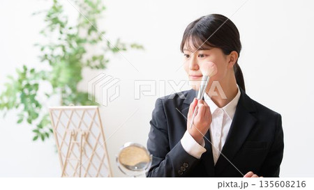 鏡を見てメイクを整えるリクルートスーツ姿の女子大学生 135608216