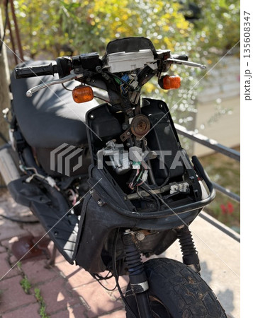 Broken motorcycle with missing front panel and exposed wiring in outdoor urban setting Broken motorcycle with missing front panel and exposed wiring in outdoor urban setting 135608347