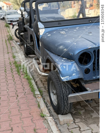 Weathered blue jeep parked on brick pavement with visible chipped paint and urban setting Weathered blue jeep parked on brick pavement with visible chipped paint and urban setting 135608348