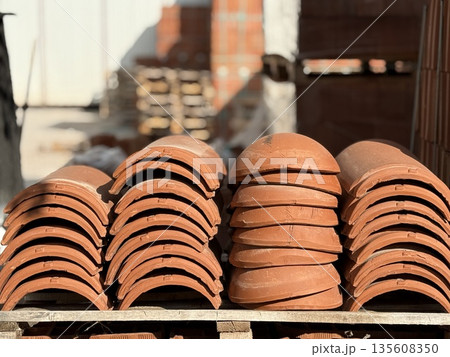 Stacked terracotta roof tiles on pallets in a sunny outdoor construction site Stacked terracotta roof tiles on pallets in a sunny outdoor construction site 135608350