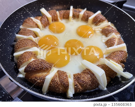 Simit ring with eggs and cheese in frying pan, breakfast dish, top view 135608363