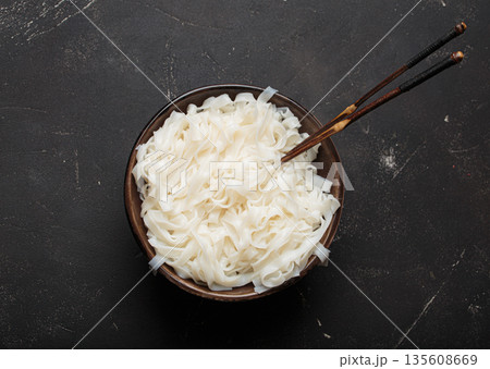 Rice cooked plain noodles with chopsticks dark bowl top view black rustic background 135608669
