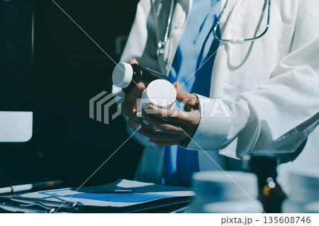 Two doctors and a female nurse meet at a table in the hospital, collaborating on medical tasks using laptops and computers 135608746