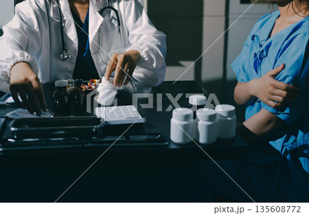 Female doctor holding a medicine bottle is checking the quality of medicine for any side effects the patient or not and recording patient information at the hospital. medical and health care concept 135608772