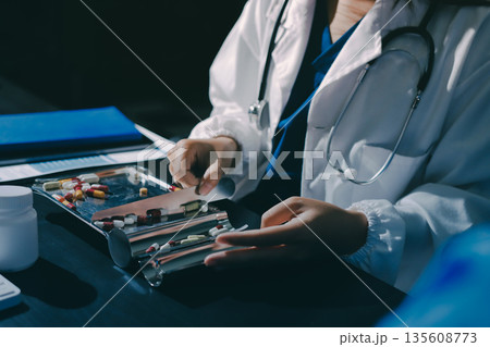 Female doctor holding a medicine bottle is checking the quality of medicine for any side effects the patient or not and recording patient information at the hospital. medical and health care concept Female doctor holding a medicine bottle is checking the quality of medicine for any side effects the patient or not and recording patient information at the hospital. medical and health care concept 135608773