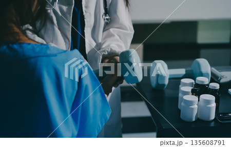 Physical therapist assisting a woman with dumbbell exercise Physical therapist assisting a woman with dumbbell exercise 135608791
