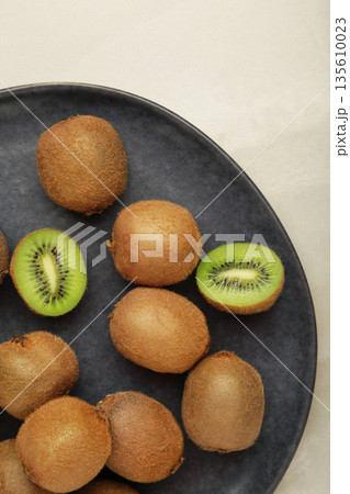Green kiwi on plate on light background. Tropical fruit. Vertical photo Green kiwi on plate on light background. Tropical fruit. Vertical photo 135610023