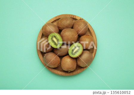Green kiwi on wooden plate on mint background. Tropical fruit. 135610052