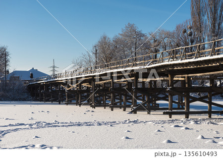 Beautiful winter landscape with a frozen pond and snow-covered wooden bridge on a clear sunny day Beautiful winter landscape with a frozen pond and snow-covered wooden bridge on a clear sunny day 135610493