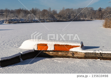 There is an overturned boat covered in snow lying on the pier. There is an overturned boat covered in snow lying on the pier. 135610498