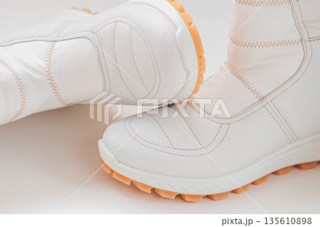 Pair of stylish white winter boots with orange soles placed on white background, showing stitched contours. Concept of modern symmetry, Cloud Dancer trend and sleek urban fashion Pair of stylish white winter boots with orange soles placed on white background, showing stitched contours. Concept of modern symmetry, Cloud Dancer trend and sleek urban fashion 135610898