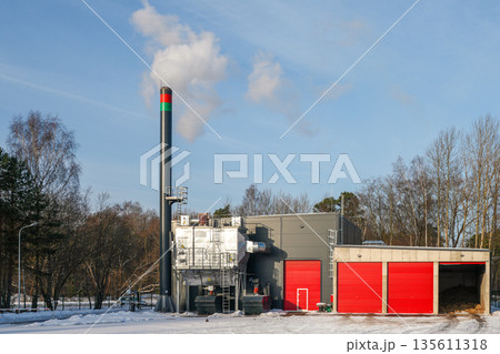 Modern biomass boiler house with wood chip heating plant and smokestack in winter Modern biomass boiler house with wood chip heating plant and smokestack in winter 135611318