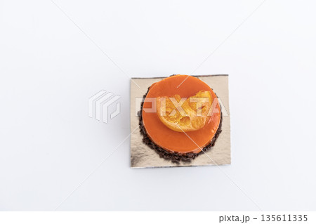 Orange colored pastry with smooth glaze and a fresh orange slice on top, citrus dessert concept Orange colored pastry with smooth glaze and a fresh orange slice on top, citrus dessert concept 135611335