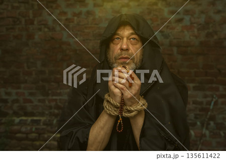 Monk holds rosary with bound hands and raises gaze during prayer. Monk holds rosary with bound hands and raises gaze during prayer. 135611422