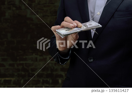 A businessman in a formal suit holding a stack of US dollars against a brick wall A businessman in a formal suit holding a stack of US dollars against a brick wall 135611427