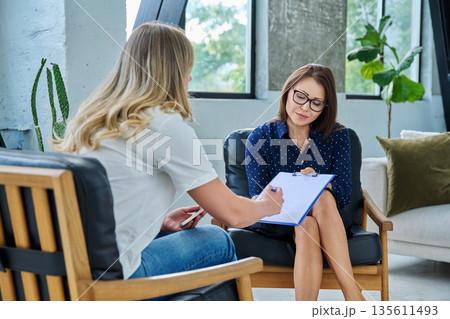 Middle aged professional female psychologist, counselor working with young woman Middle aged professional female psychologist, counselor working with young woman 135611493