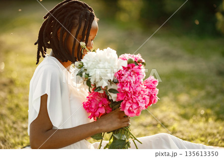 Romantic picnic. Beautiful african american woman sitting alone and sniffing flowers. Summer time. 135613350