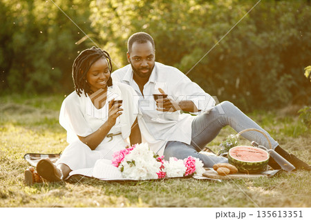 Carefree, relaxed couple enjoying the picnic together. Man and woman tasting red wine from glasses. 135613351