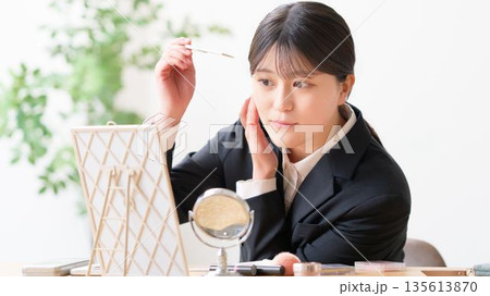 鏡を見ながらコームで前髪を整えて身だしなみチェックをするリクルートスーツ姿の女性 135613870