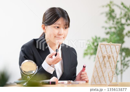 鏡を見てメイクを整えるリクルートスーツ姿の女子学生 135613877