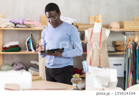 African American man tailor creates sketch of dress on tablet African American man tailor creates sketch of dress on tablet 135614104