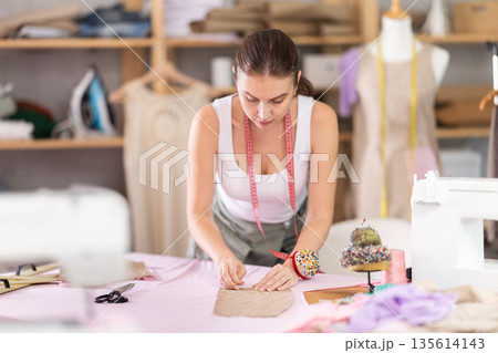 Woman seamstress works with pattern and fabric Woman seamstress works with pattern and fabric 135614143