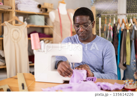 Male clothing designer stitching fabric on sewing machine in studio Male clothing designer stitching fabric on sewing machine in studio 135614226