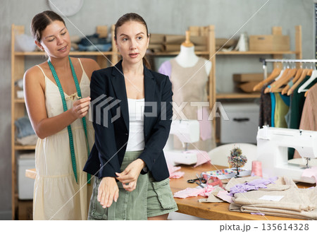 woman dressmaker offers a client a sewn jacket in a workshop woman dressmaker offers a client a sewn jacket in a workshop 135614328