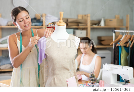Atelier Worker Sewing Clothes Next to Dressmaker Atelier Worker Sewing Clothes Next to Dressmaker 135614362