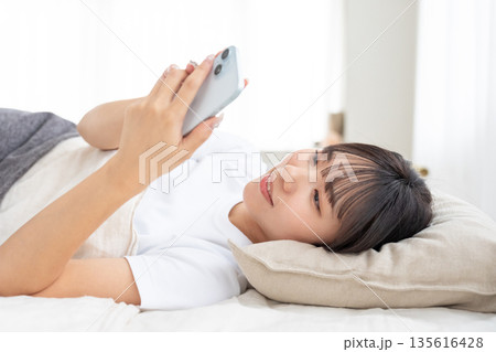 ベッドでスマホを操作する若い女性 ベッドでスマホを操作する若い女性 135616428