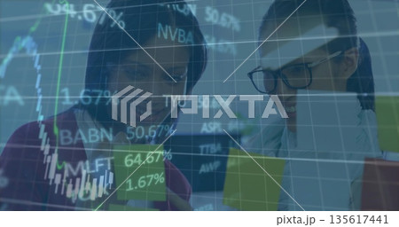 Financial analysts wearing business attire studying stocks on tablet in office, with ticker overlay 135617441