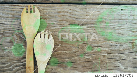 Two bamboo slotted spoons resting left side on kitchen table with green paint stains, copy space 135617703
