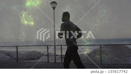 Running mid-adult man moving along seaside promenade at dawn, with metal railing and lamppost Running mid-adult man moving along seaside promenade at dawn, with metal railing and lamppost 135617742